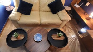Una sala moderna con un sofá color beige, dos mesitas auxiliares negras con jarrones decorativos y una mesa de centro de madera.