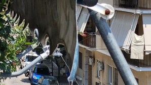 Un edificio de varios pisos con balcones, una calle con autos estacionados y un cielo despejado.