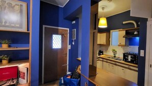 Una cocina pequeña con microondas, estufa y lavamanos. Se observa una pared azul y una puerta de madera.