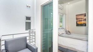 A modern bedroom with a bed, a window with a view, a small bedside table, and a grey sofa. - New modern condo 3 minute walk to West Bay Beach (West Bay)