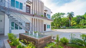 A modern two-story house with a staircase leading to a balcony, surrounded by lush greenery and a small water feature. - New modern condo 3 minute walk to West Bay Beach (West Bay)