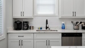 A kitchen with white cabinets, a coffee maker, a sink, and a dishwasher. - Barefoot Bliss - Single Level Steps to the Beach (Corolla)