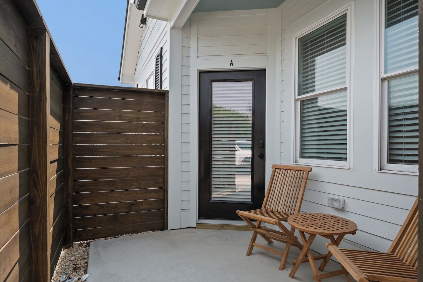 A wooden fence, a black door, and a wooden bench with a table in front of a house.