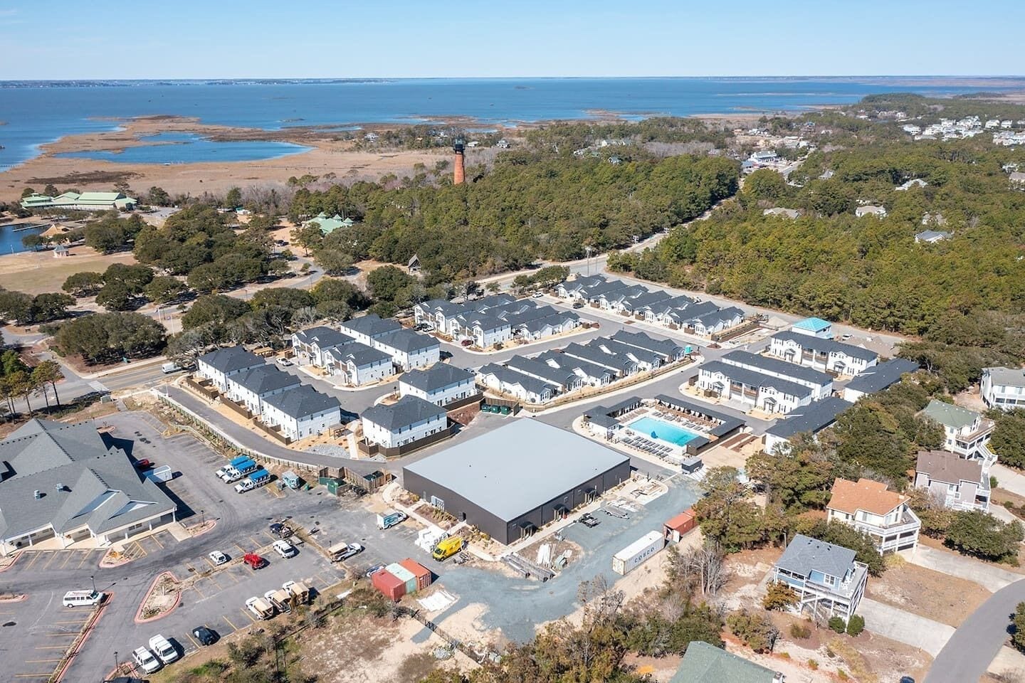 A residential area with multiple houses, a large parking lot, and a body of water in the background.