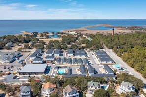 Un quartier résidentiel situé sur la côte, avec plusieurs maisons, une piscine et un phare en arrière-plan.