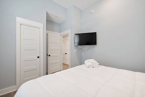 Une chambre d’hôtel avec un lit, un téléviseur fixé au mur et un ensemble de portes blanches.