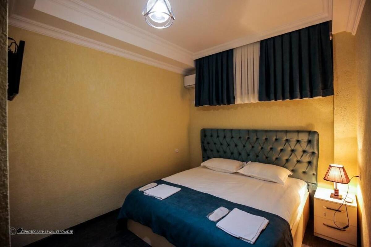 A hotel room with a single bed, a nightstand with a lamp, and a window with curtains.