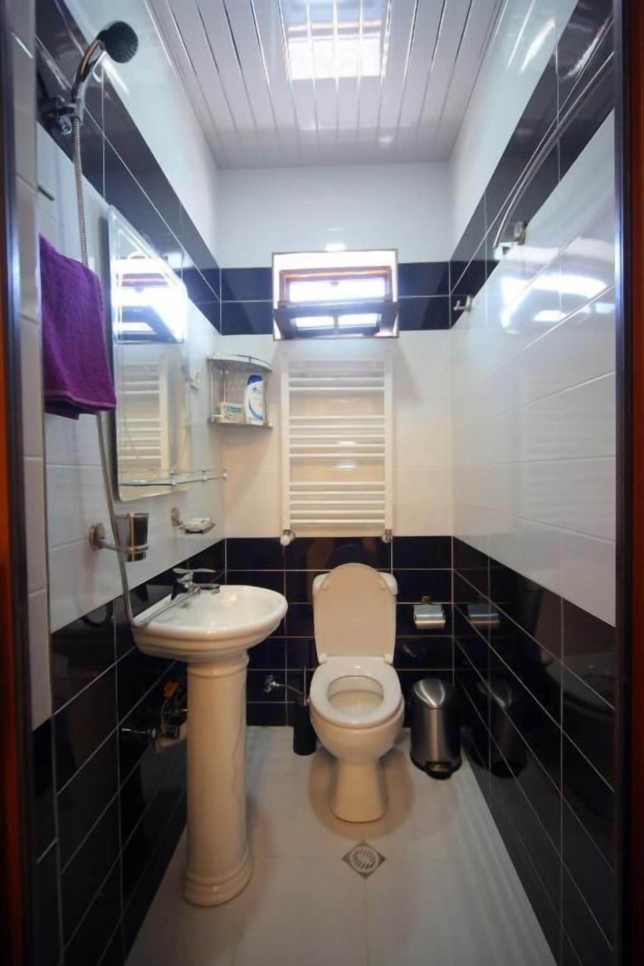 A compact bathroom with a pedestal sink, toilet, and a small window with blinds.