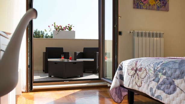 Une chambre avec un lit, une porte vitrée donnant sur un espace extérieur aménagé avec des meubles en osier et un jardinière.