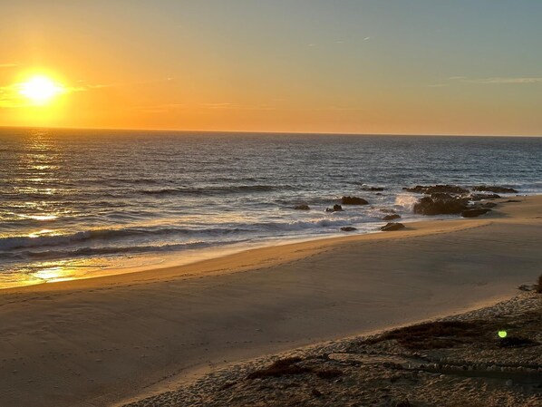 A beach with a sunset, waves, and rocks.