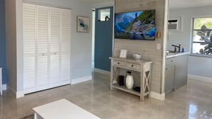 A modern living room with a TV, a white bench, a wooden console table, and a closet.