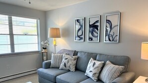A living room with a grey sofa, patterned cushions, a white coffee table, and abstract wall art.