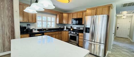 A modern kitchen with wooden cabinets, stainless steel appliances, and a large marble countertop.