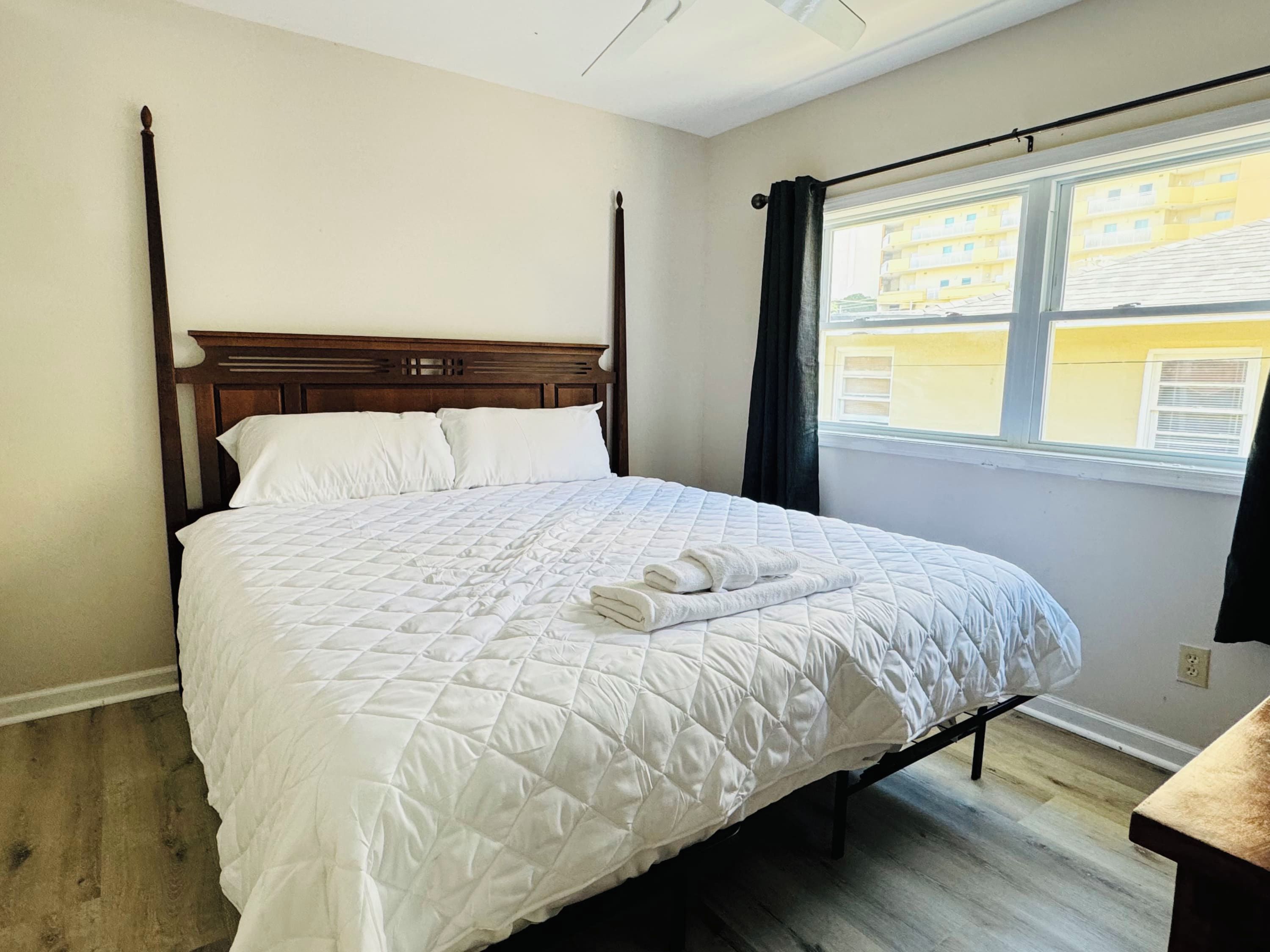A single bed with a wooden headboard, white bedding, and a window with curtains.