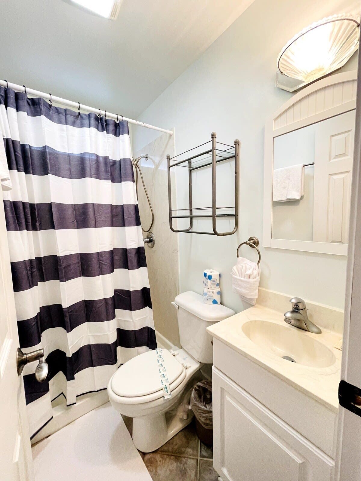 A bathroom with a striped shower curtain, a toilet, a sink with a mirror, and a towel rack.