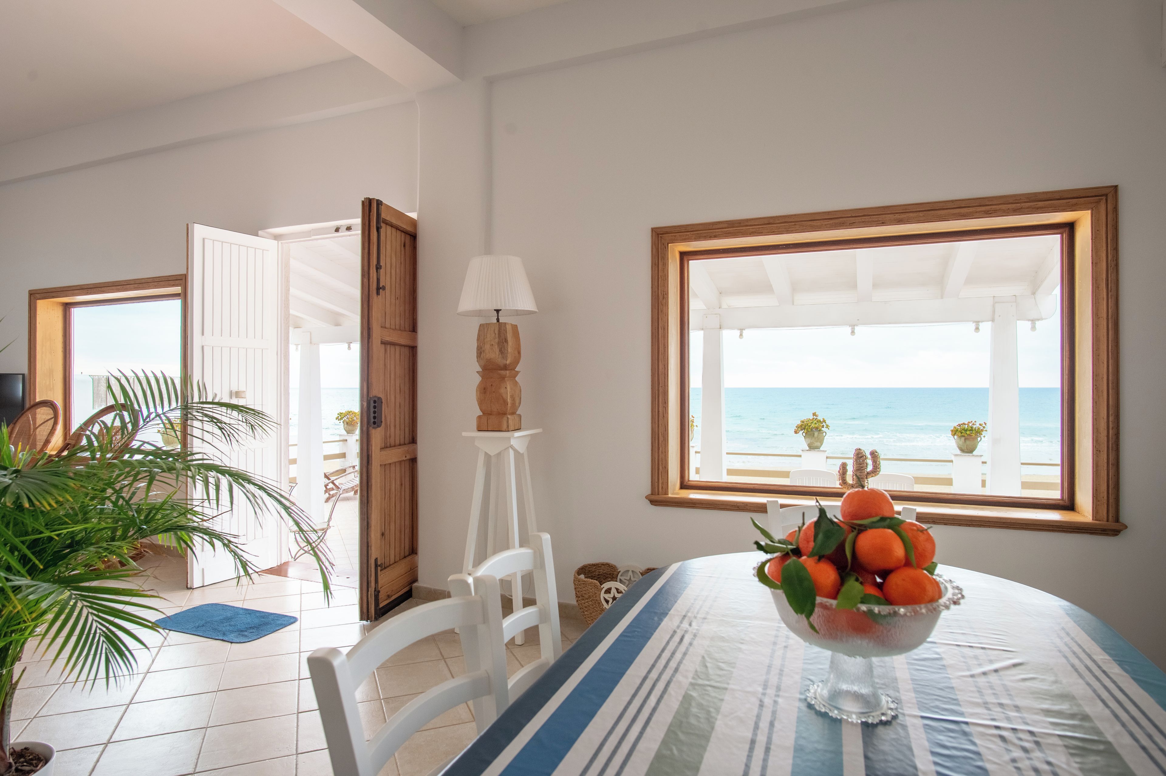 A room with a view of the sea, a table with a fruit bowl, and a lamp.