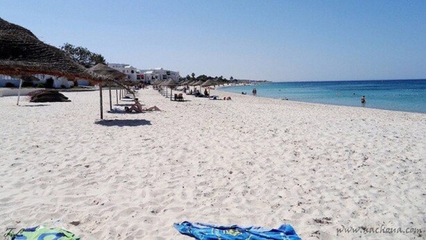 A beach with white sand, thatched umbrellas, and white buildings in the background. - Luxury Studio Apartment - Sea View In Sousse (Port El Kantaoui)