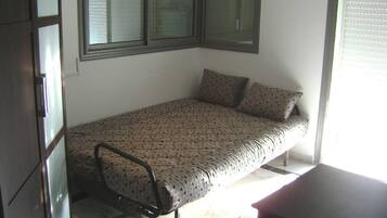 A small bedroom with a bed, a chair, a desk, and a window with blinds.