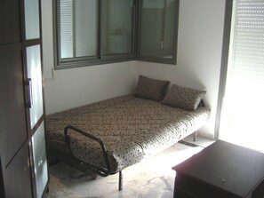 A small bedroom with a bed, a chair, a desk, and a window with blinds. - Luxury Studio Apartment - Sea View In Sousse (Port El Kantaoui)