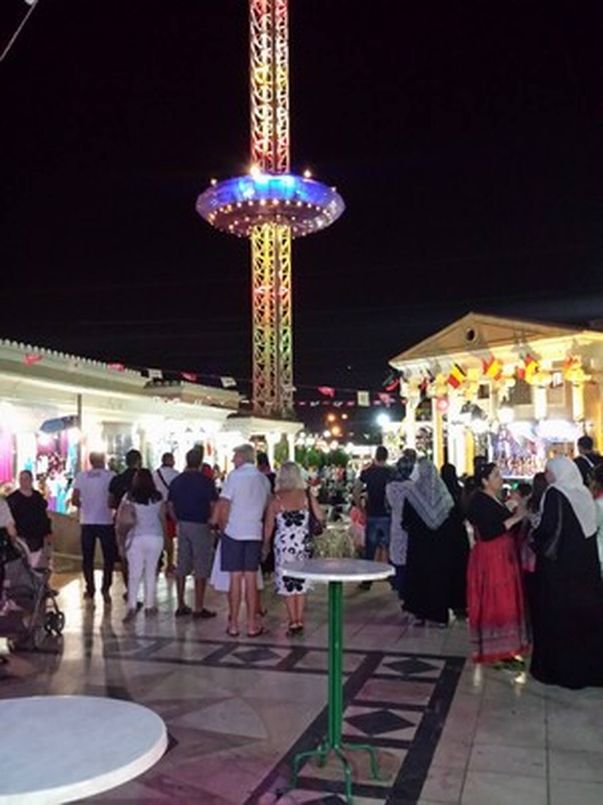 A public square with a tall, brightly lit tower and a small table in the foreground.