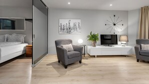 A modern living room with a sofa, armchair, TV, lamp, and artwork.