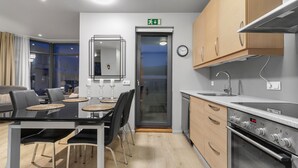 A modern kitchen with a built-in oven, a dining area with a glass table and chairs, and a view of the city through large windows.