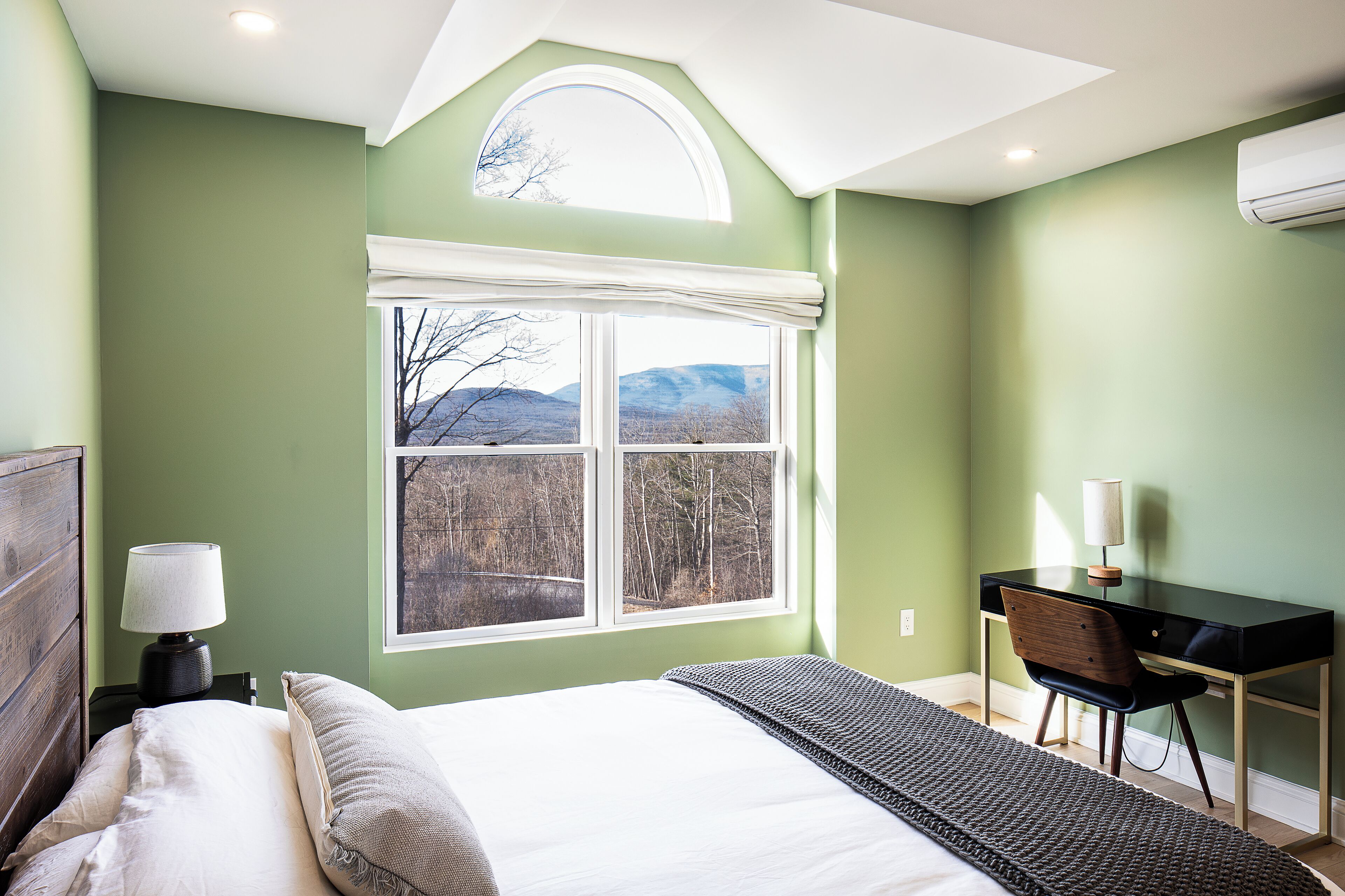 A bedroom with a bed, a desk, and a window with a view of trees and mountains.