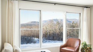 Una habitación con un ventanal grande, un sillón de cuero marrón, un sofá blanco y una planta.