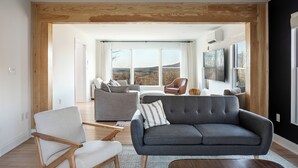 Una sala de estar moderna con un sofá gris, sillones de madera y un ventanal con vistas al exterior.