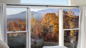 Un dormitorio con un amplio ventanal que ofrece vistas a follaje otoñal y montañas.