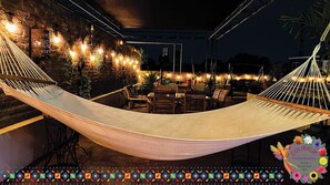 Un espacio de estar al aire libre con una hamaca, sillas de madera y mesas.