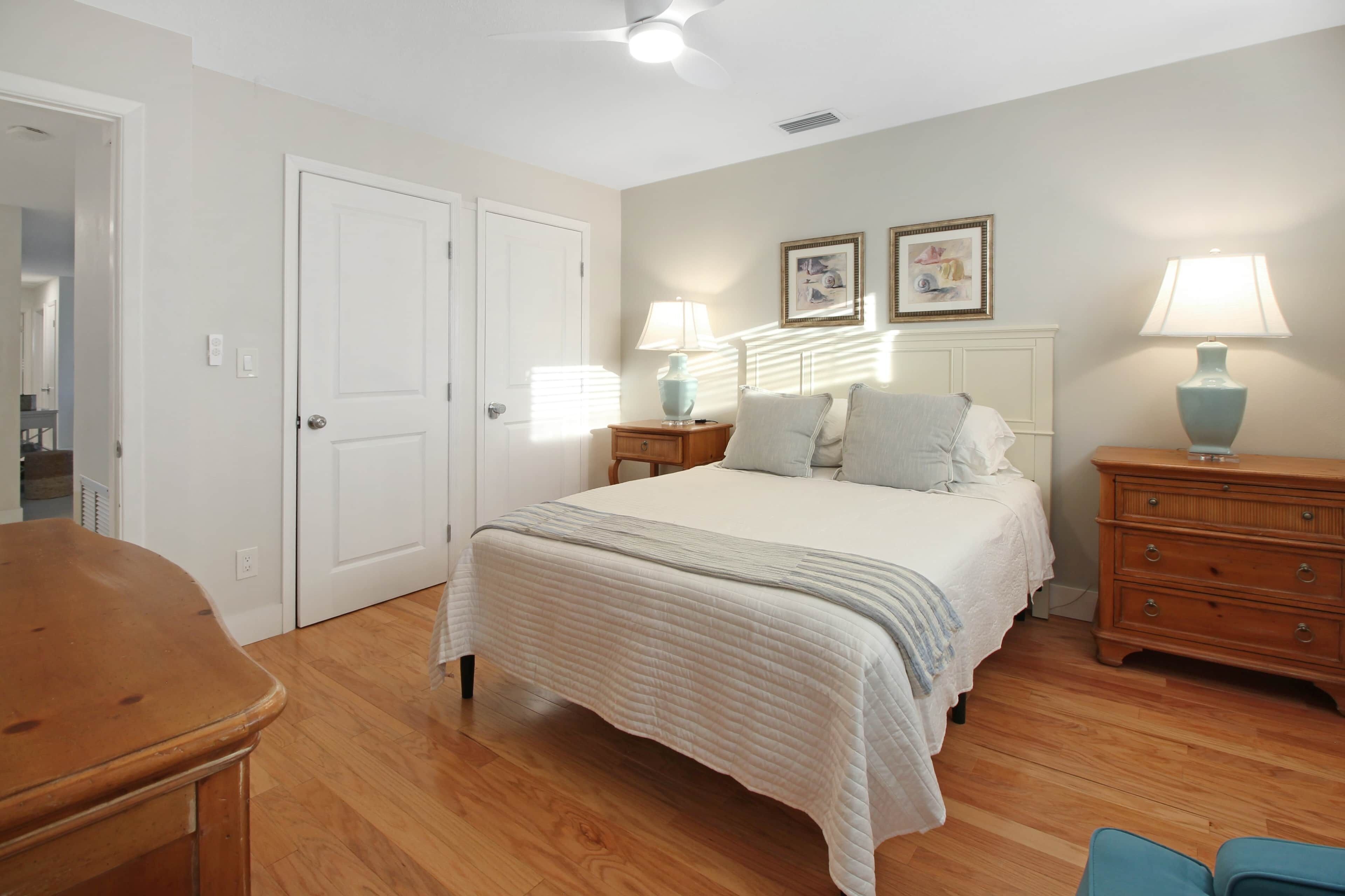 Un dormitorio con cama, dos mesitas de noche con lámparas, cómoda y una puerta.