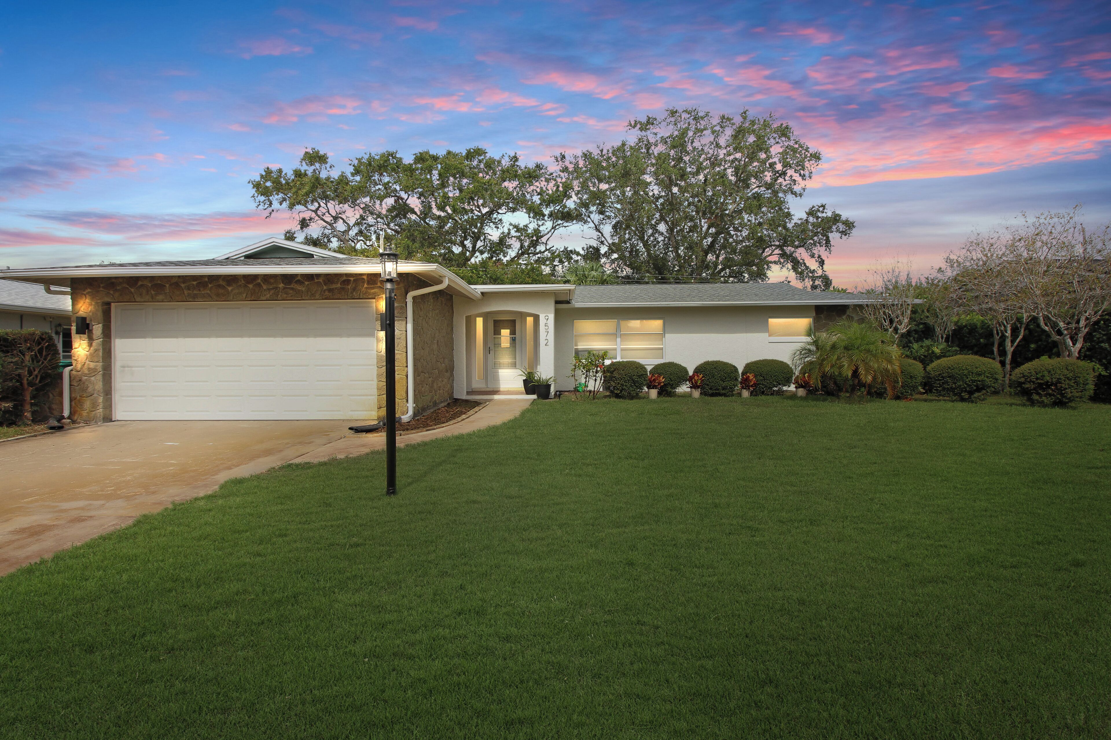 A modern two-story house with a garage, a well-maintained lawn, and a large tree in the backyard.