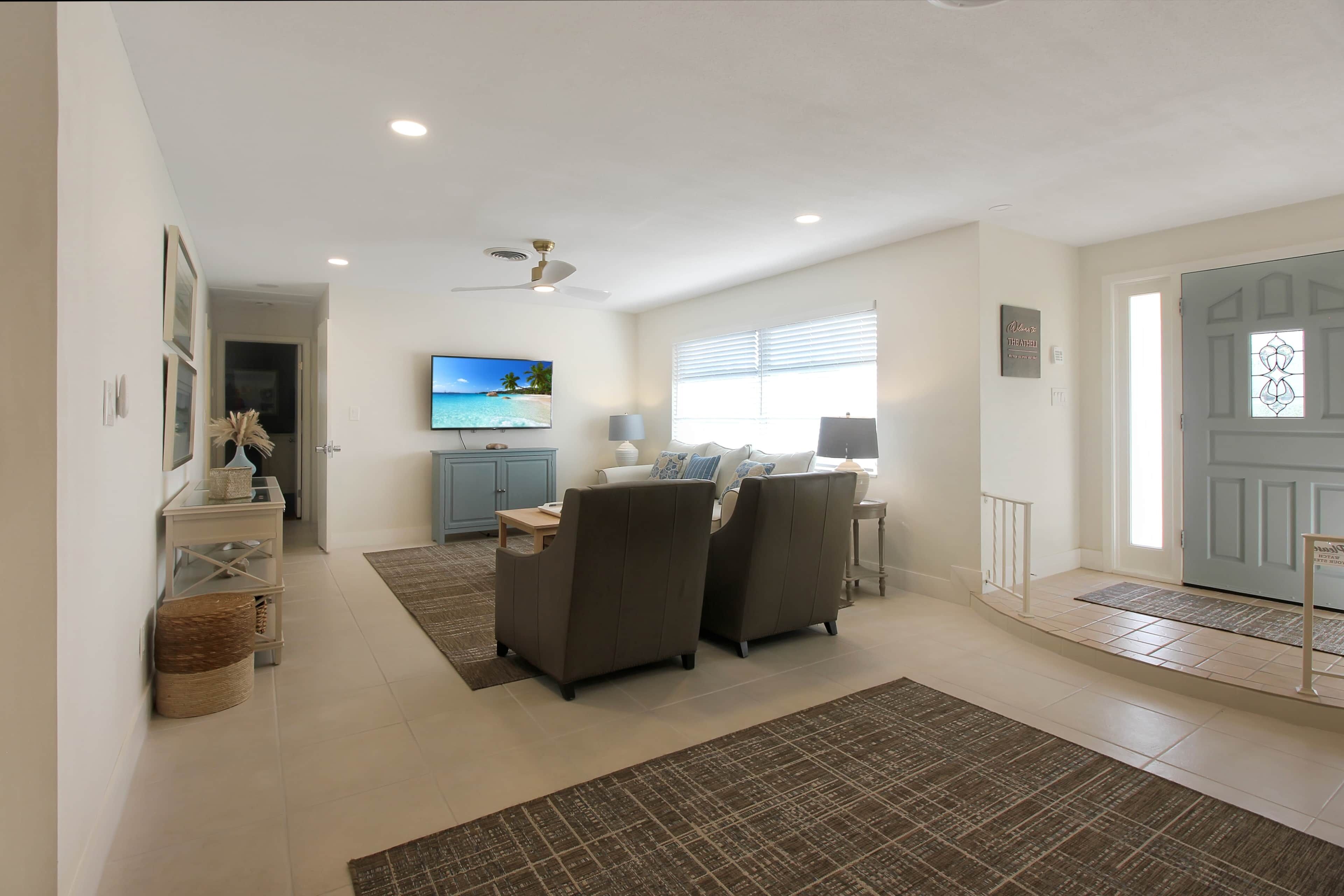 A spacious living room with a flat-screen TV, grey sofas, a coffee table, and a ceiling fan.