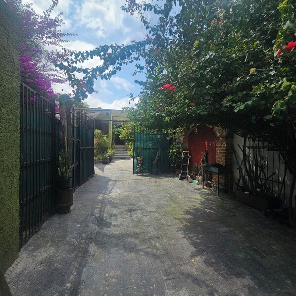 A narrow alleyway with a green gate, a brick wall, and a red archway.