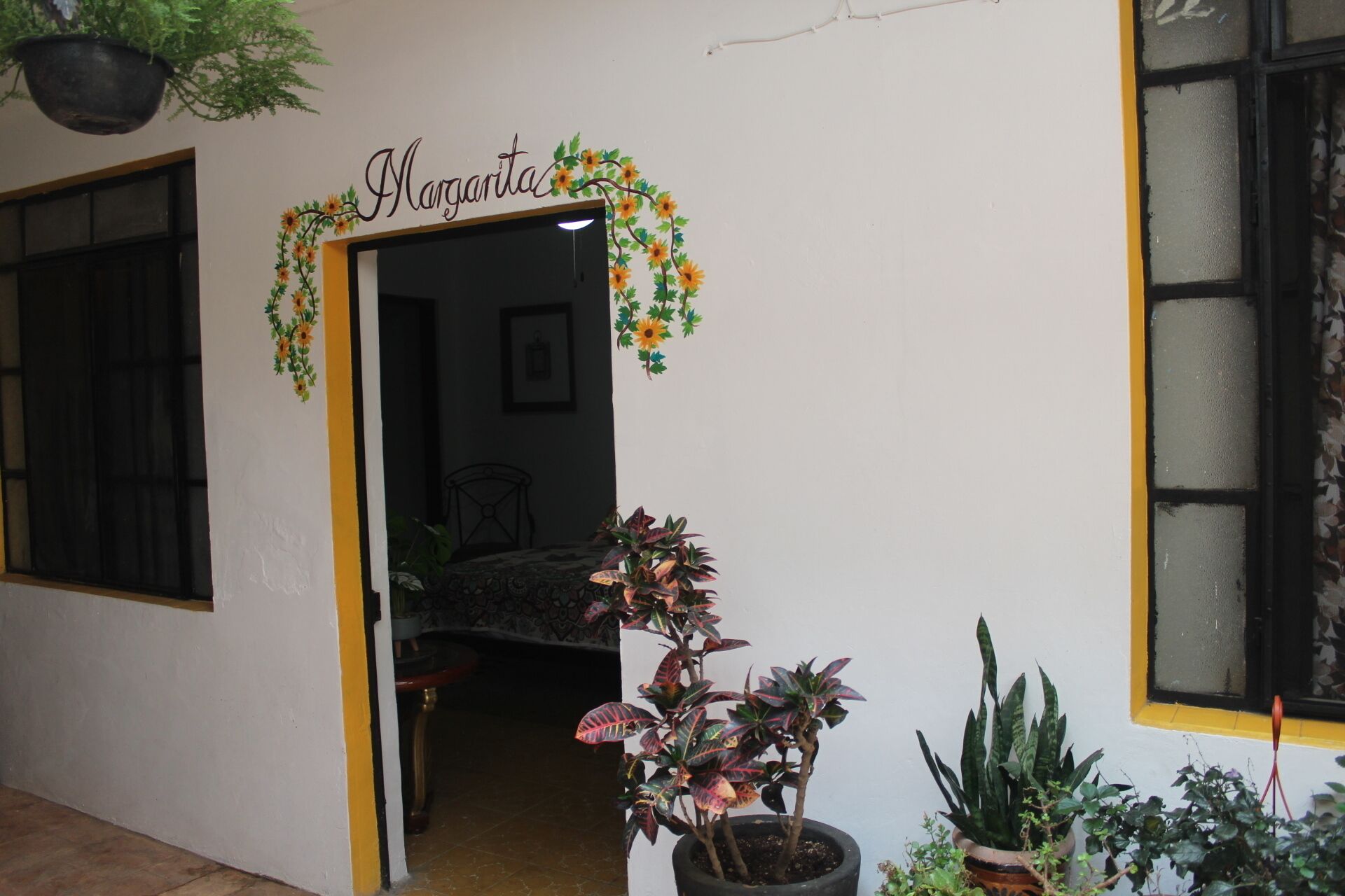 A doorway with a sign reading "Margarita," a potted plant, and a window with yellow trim.