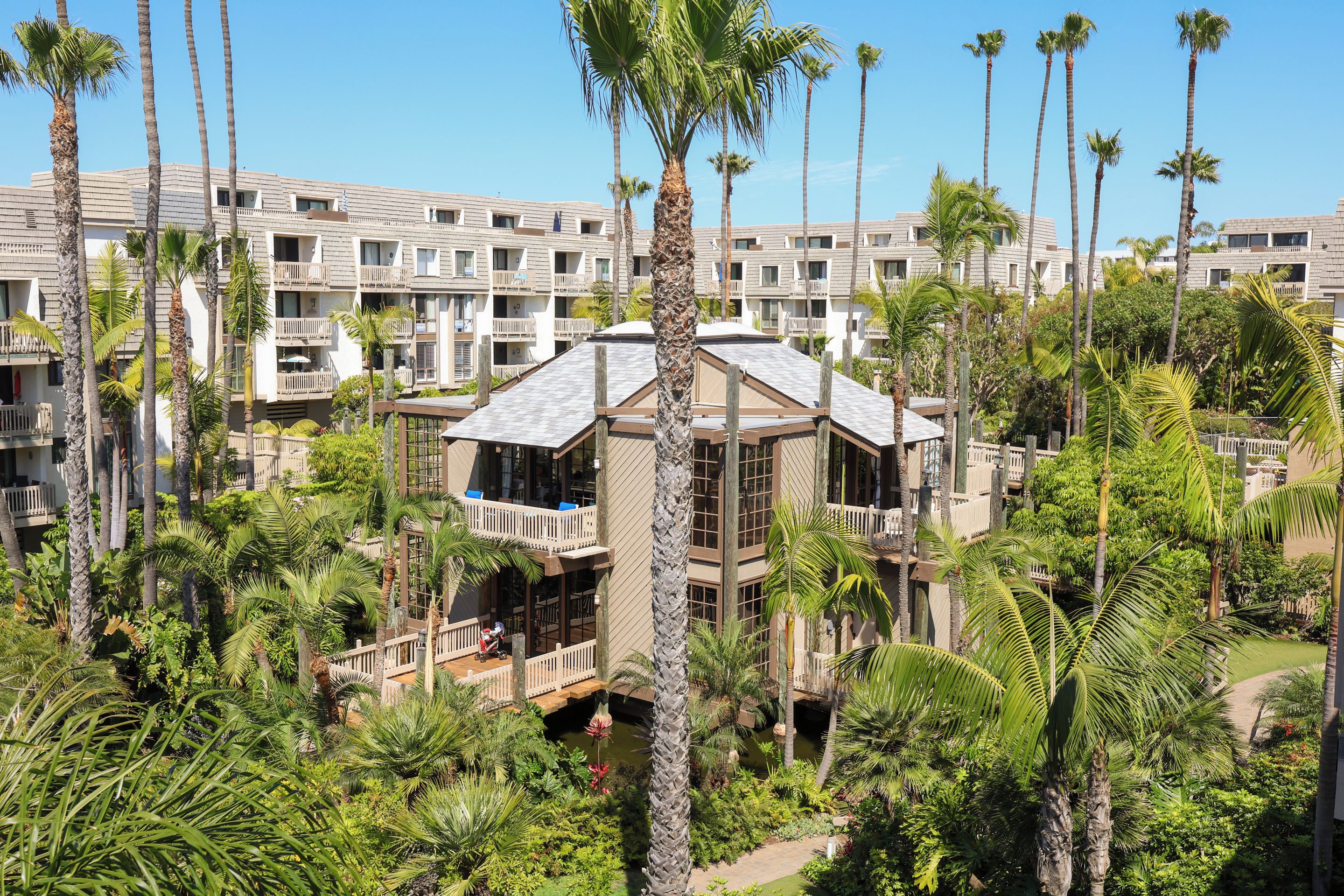 A hotel with multiple floors, balconies, and lush greenery including palm trees.