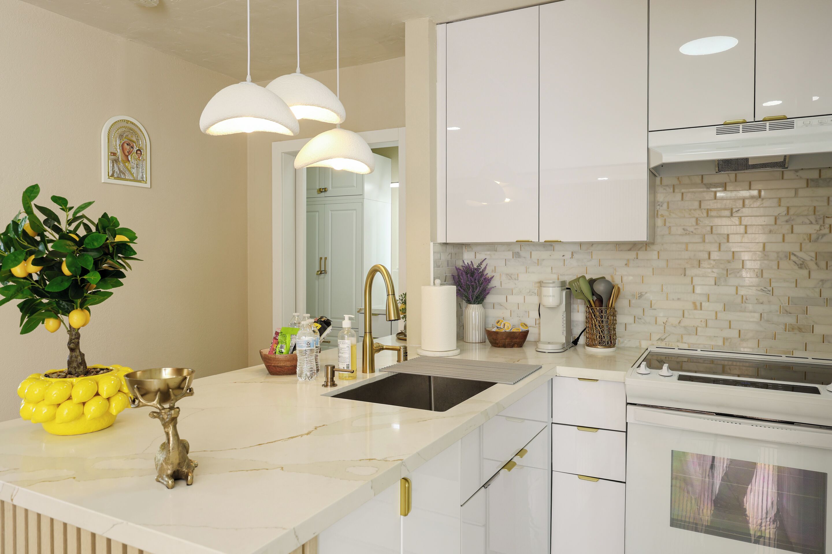 A modern kitchen with white cabinetry, a marble countertop, a sink, and a stove.