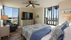 Ein Schlafzimmer mit einem großen Bett, einem Fernseher, einem Schreibtisch und Blick aufs Meer.