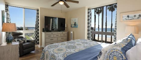 A bedroom with a large bed, a TV, a desk, and a view of the ocean.
