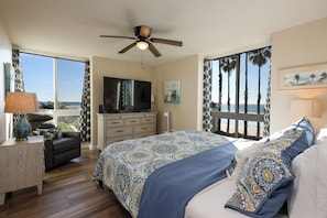 A bedroom with a large bed, a TV, a desk, and a view of the ocean. - Oceanside Beach Condos (Oceanside)
