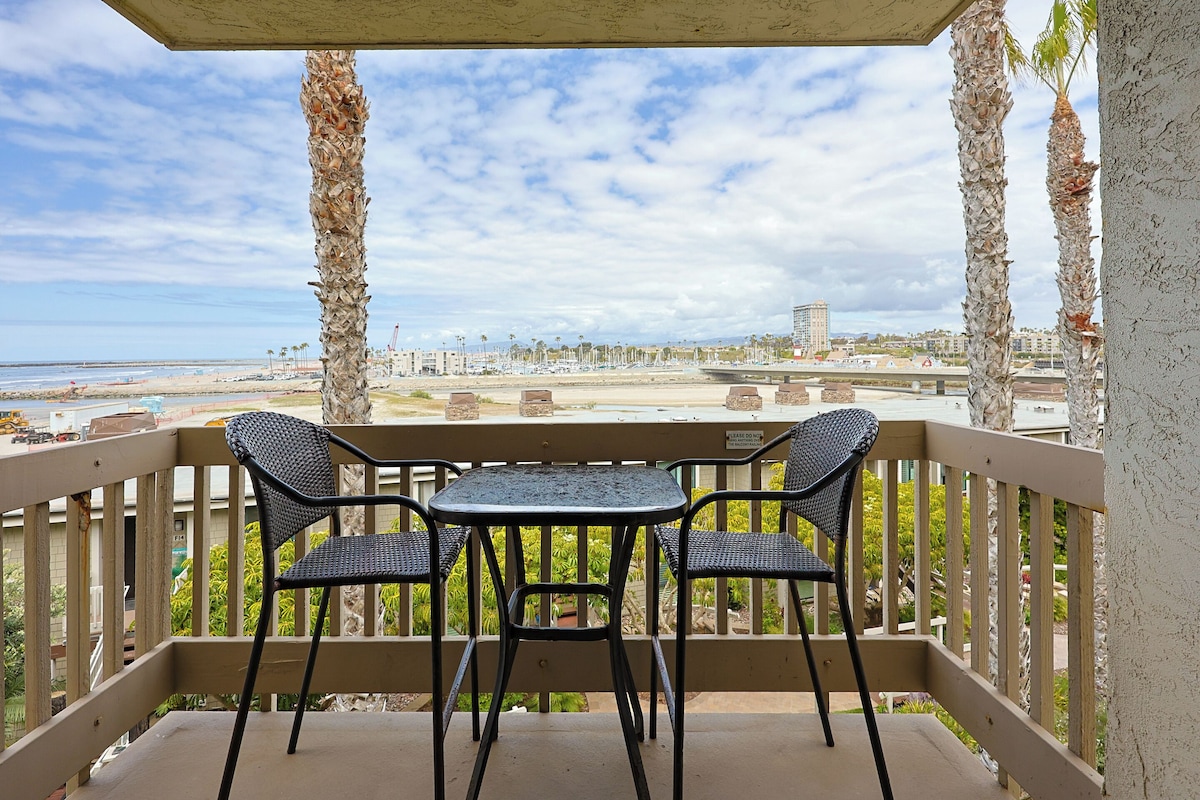 Balcón con dos sillas y una mesa, con vista a la playa y al paisaje urbano.