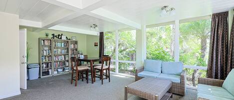 A spacious living area with a large bookshelf, a dining table, and a comfortable seating area with a view of the outdoors.