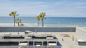 Eine Dachterrasse mit Solaranlagen, einer Betonbarriere und Palmen am Meer.