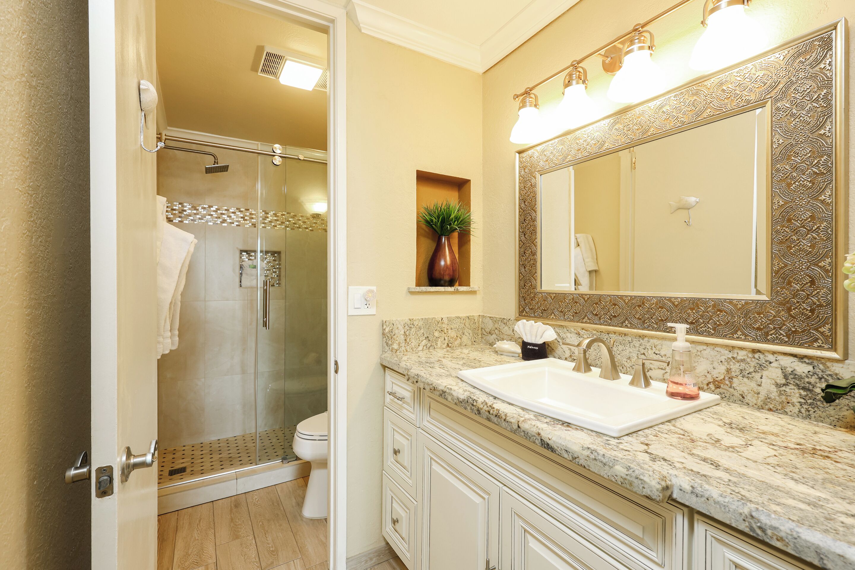Un bagno con box doccia in vetro, un lavabo con piano in marmo e un grande specchio con decorazioni elaborate.