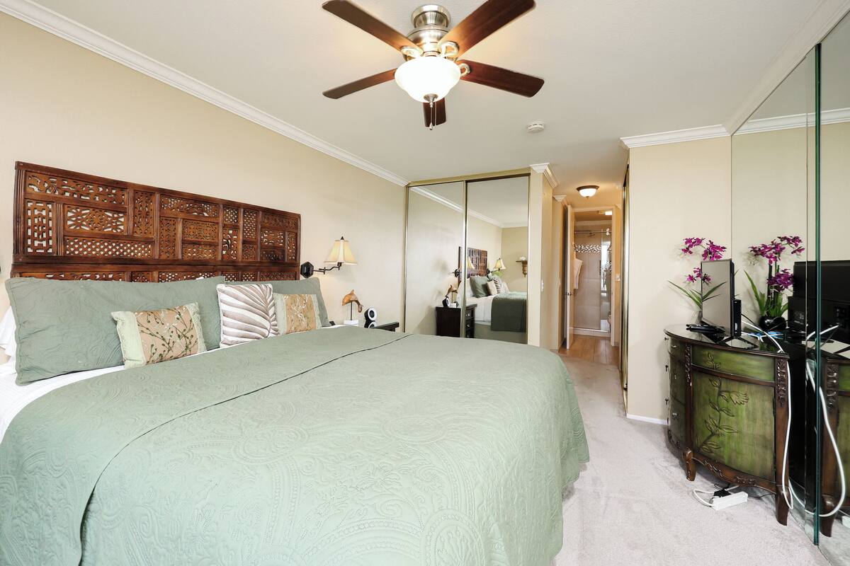 A bedroom with a large bed, a ceiling fan, a dresser, and a mirror.