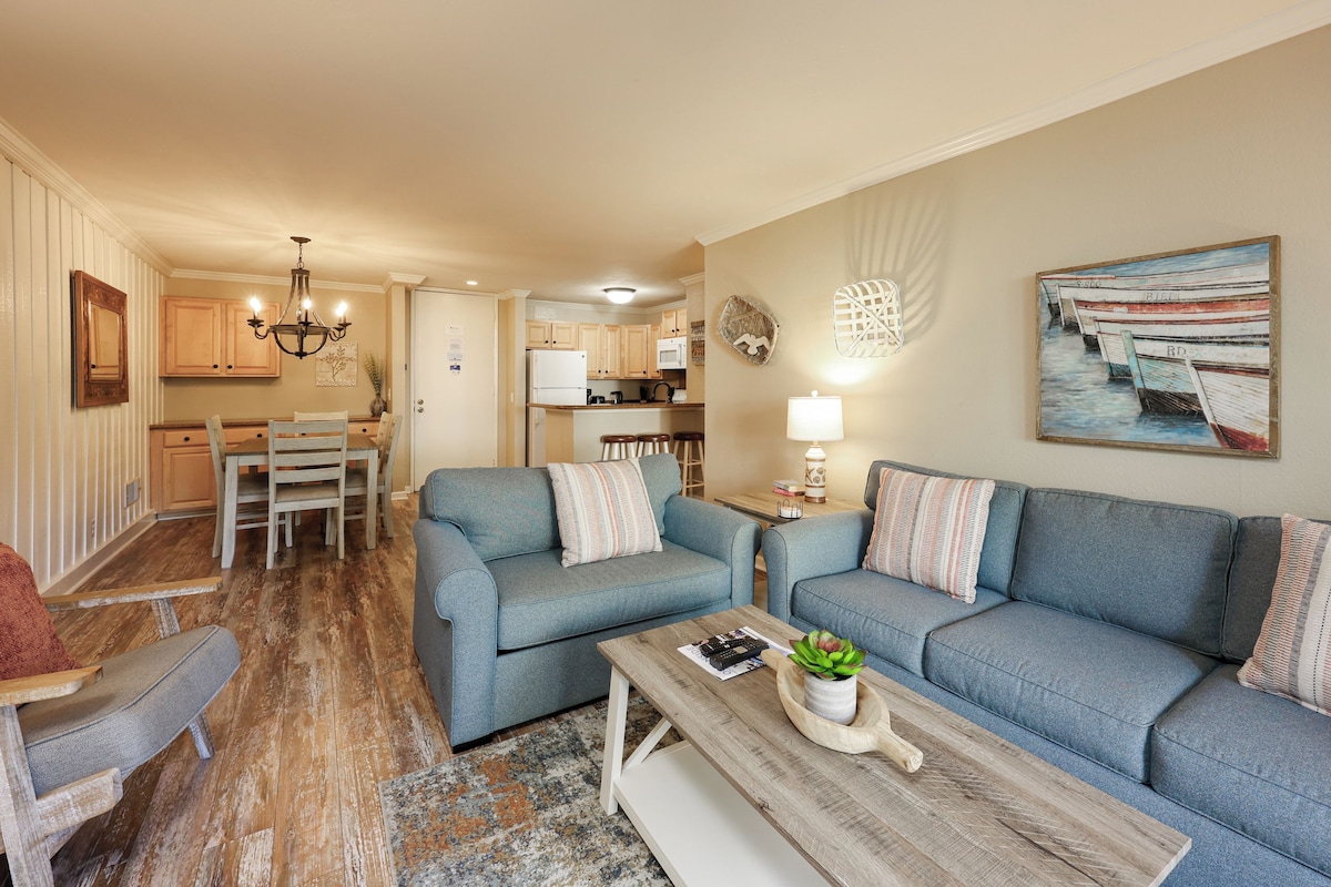 A living room with a blue sofa set, a wooden coffee table, and a dining area with a wooden table and chairs.