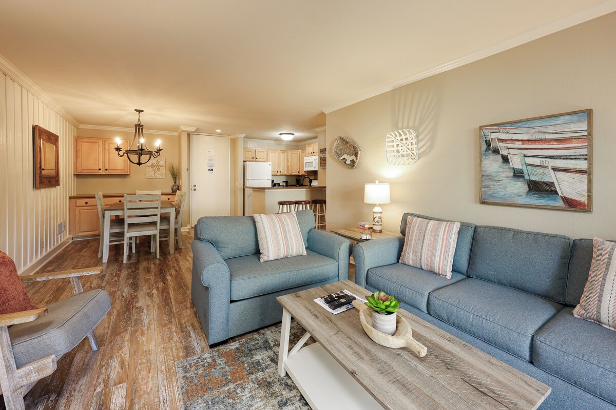 A living room with a blue sofa set, a wooden coffee table, and a dining area with a wooden table and chairs.