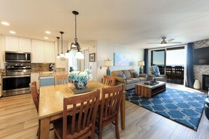 A modern kitchen with stainless steel appliances, a dining area with wooden furniture, and a living room with a fireplace and large windows. - Oceanside Beach Condos (Oceanside)