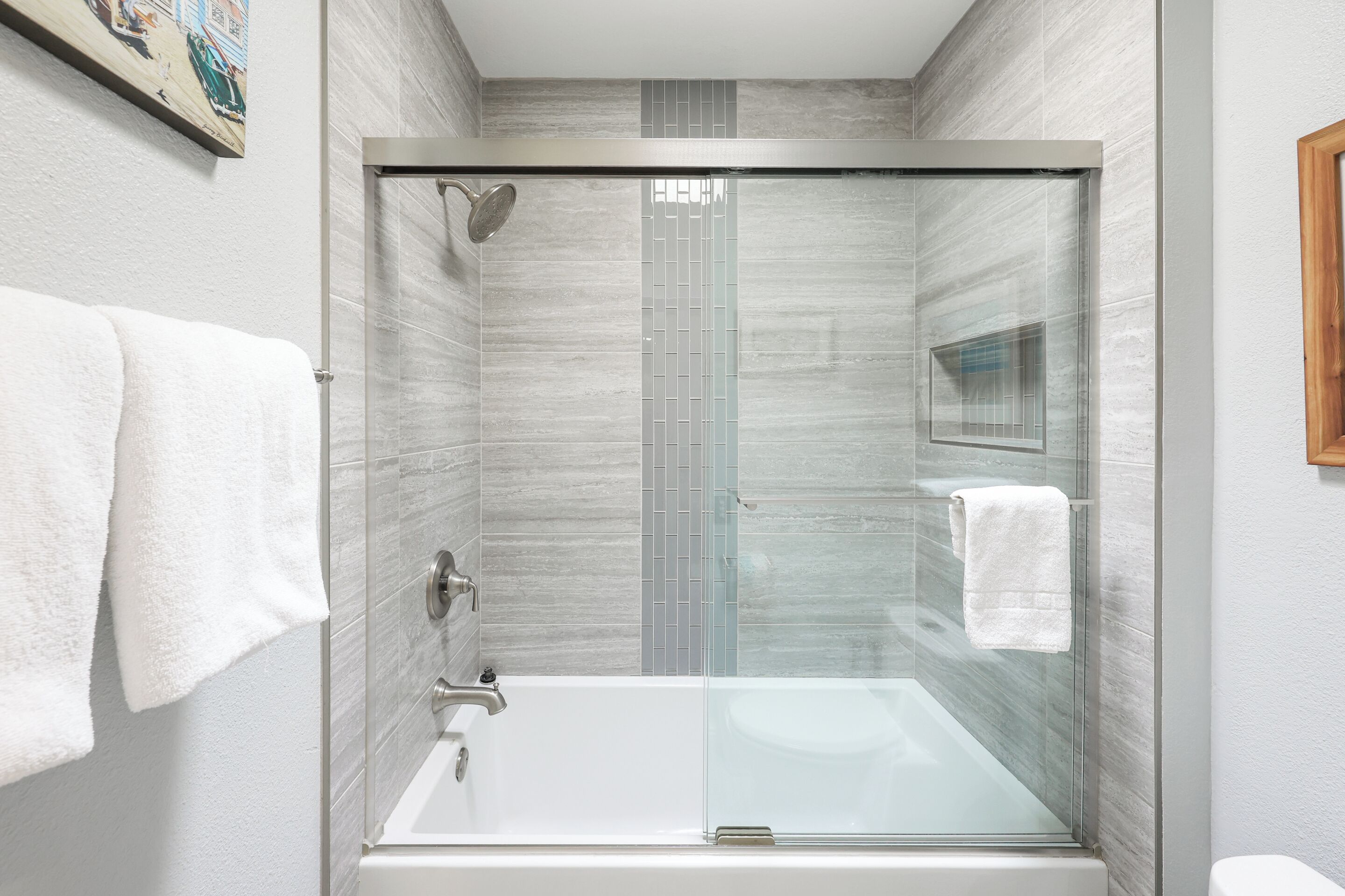 A modern bathroom with a glass-enclosed shower, a white bathtub, and a tiled wall.